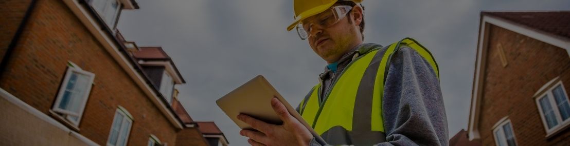 Utility field worker wearing high visibility clothing looking at a tablet device outside with houses in the background